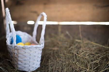 Easter eggs in a basket on a hay with a blurred background.