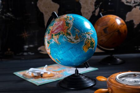 Globe with a barometer and a small plane on the background of a black world map.の写真素材