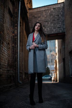 Girl in a red blouse and a gray cardigan on the background of the old brick wall.の写真素材