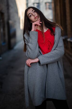 Girl in a red blouse and a gray cardigan on the background of the old brick wall.の写真素材