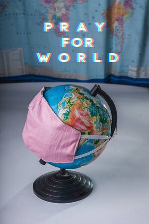 Globe in a medical mask on the background of a blurred world map with the inscription Pray for...