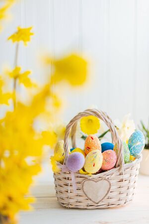 Multi-colored Easter eggs in a basket on a white wooden background.の写真素材