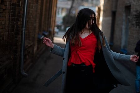 Girl in a red blouse and a gray cardigan on the background of the old brick wall.の写真素材