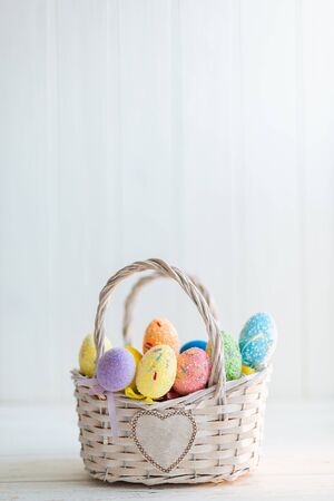 Multi-colored Easter eggs in a basket on a white wooden background.の写真素材
