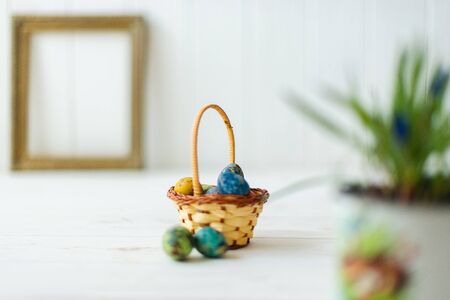 Multi-colored Easter eggs in a basket on a white wooden background.の写真素材