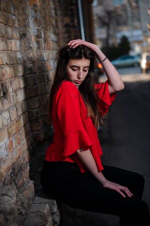 Girl in a red blouse and a gray cardigan on the background of the old brick wall.の写真素材