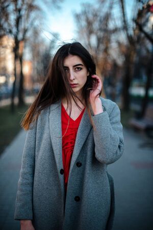 Girl in a red blouse and a gray cardigan on a blurry city background in early spring.