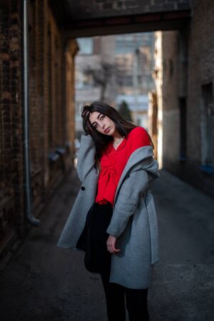 Girl in a red blouse and a gray cardigan on the background of the old brick wall.の写真素材