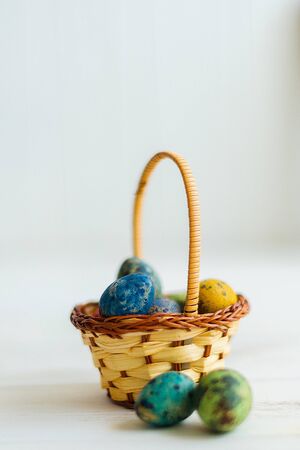 Multi-colored Easter eggs in a basket on a white wooden background.の写真素材