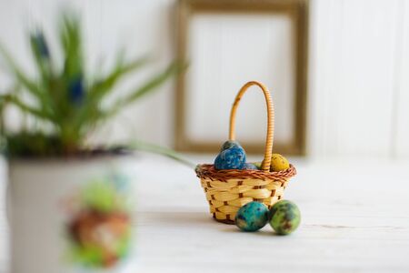Multi-colored Easter eggs in a basket on a white wooden background.の写真素材