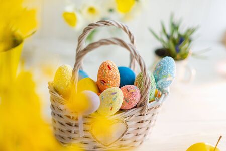 Multi-colored Easter eggs in a basket on a white wooden background.の写真素材