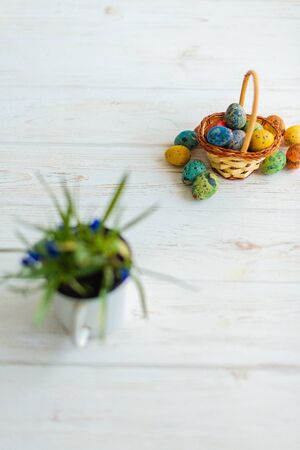 Multi-colored Easter eggs in a basket on a white wooden background.の写真素材