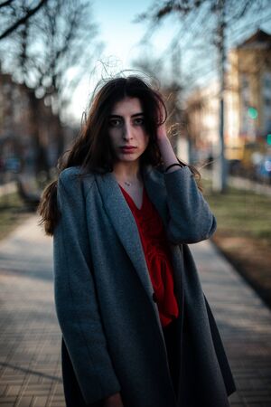 Girl in a red blouse and a gray cardigan on a blurry city background in early spring.の写真素材