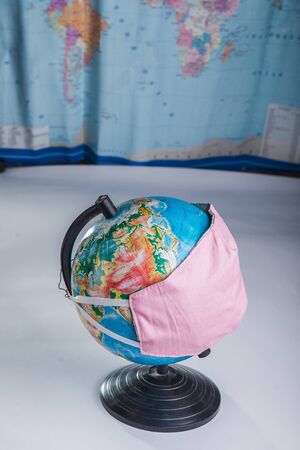 Globe in a medical mask on the background of a blurred world map concept of the global pandemic.の写真素材