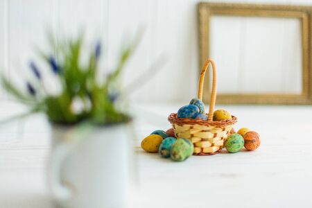 Multi-colored Easter eggs in a basket on a white wooden background.の写真素材