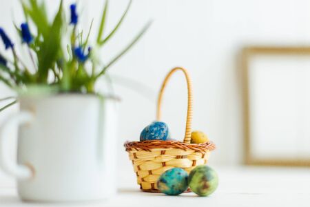 Multi-colored Easter eggs in a basket on a white wooden background.