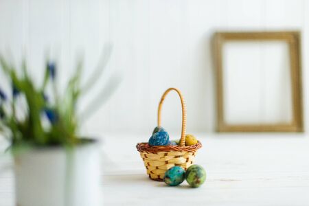 Multi-colored Easter eggs in a basket on a white wooden background.の写真素材