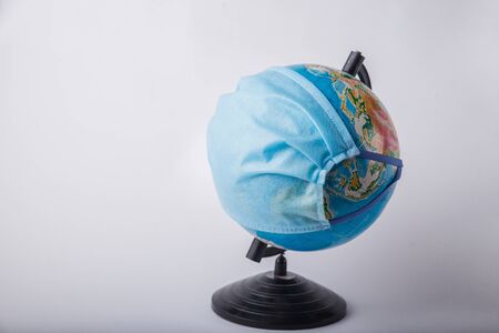 Globe in a medical mask on a light blurry background. Coronavirus pandemic protection concept.の写真素材