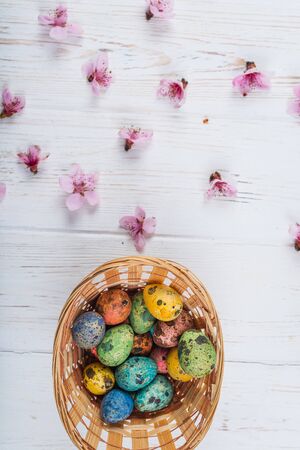 Multi-colored Easter eggs in a basket on a white wooden background.の写真素材