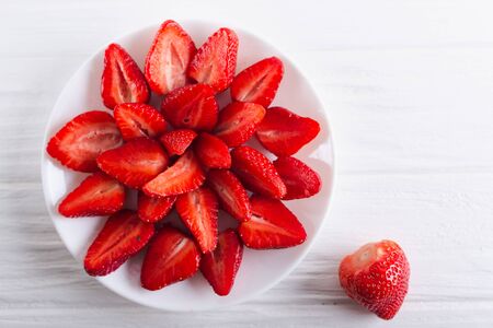 Juicy fresh sliced strawberries on a white plate on a white wooden background.の写真素材