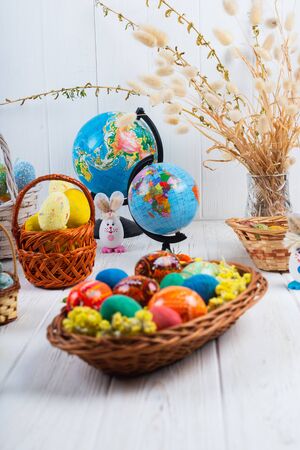 Multi-colored Easter eggs in a basket on a white wooden background.の写真素材