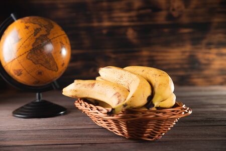 Bananas in a basket on a wooden brown natural background near a brown globe.の写真素材