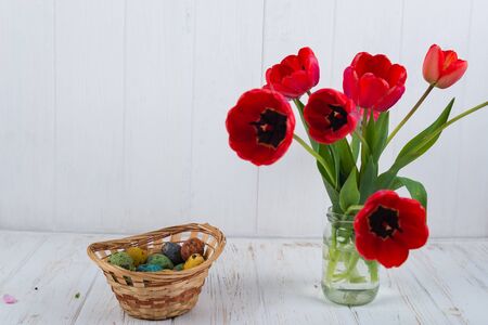 Multi-colored Easter eggs in a basket on a white wooden background.の写真素材