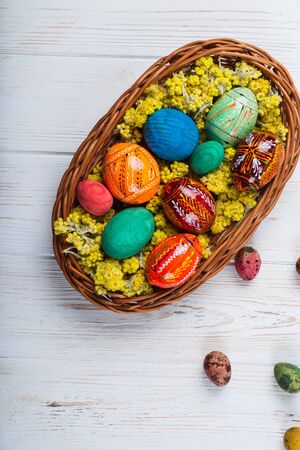 Multi-colored Easter eggs in a basket on a white wooden background.の写真素材