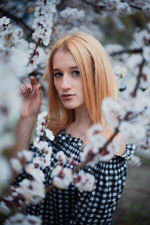 Beautiful young blonde girl on a background of flowering trees.の写真素材