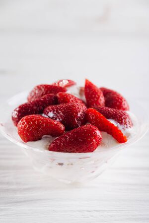 Strawberry dessert in a plate with ice cream and cream on a white wooden background.の写真素材