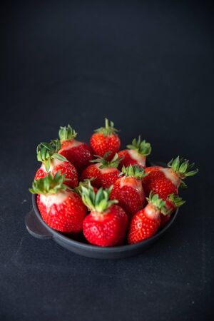 Fresh juicy strawberries in a black plate on a black matte background.の写真素材