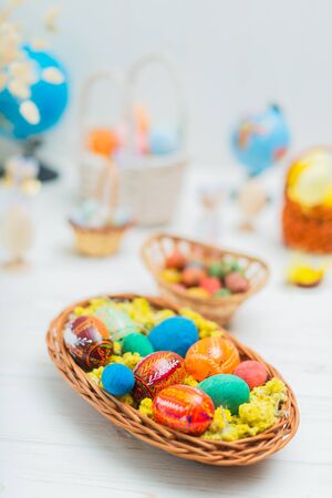 Multi-colored Easter eggs in a basket on a white wooden background.の写真素材