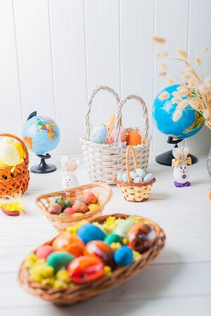 Multi-colored Easter eggs in a basket on a white wooden background.の写真素材