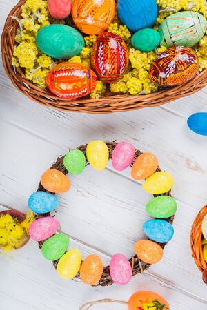 Multi-colored Easter eggs in a basket on a white wooden background.の写真素材