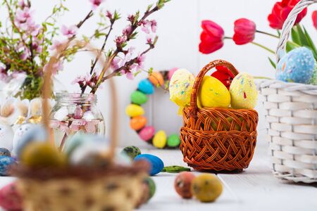 Multi-colored Easter eggs in a basket on a white wooden background.