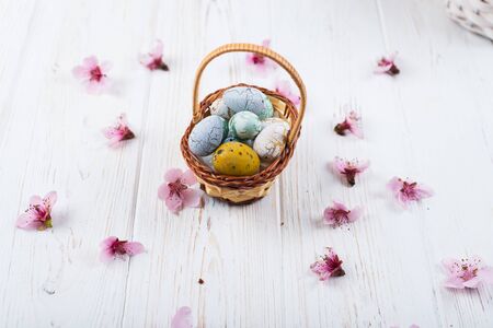 Multi-colored Easter eggs in a basket on a white wooden background.の写真素材