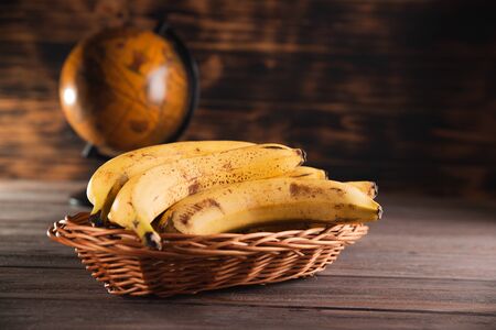 Bananas in a basket on a wooden brown natural background near a brown globe.の写真素材