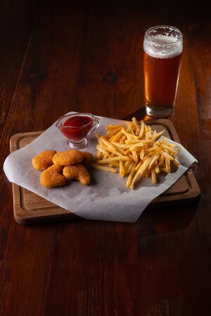 Nuggets french fries and sauce on a dark wooden background with beer.の写真素材