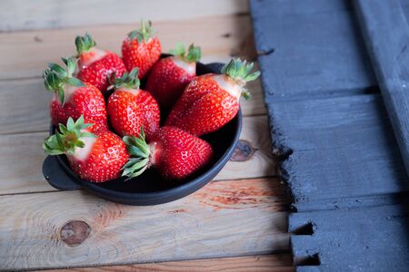 Strawberries in a black plate on a wooden background.の写真素材
