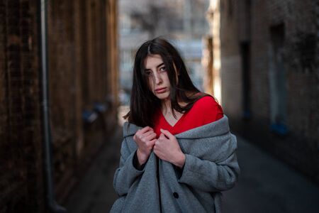 Girl in a red blouse and a gray cardigan on the background of the old brick wall.の写真素材