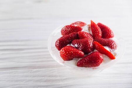 Strawberry dessert in a plate with ice cream and cream on a white wooden background.の写真素材