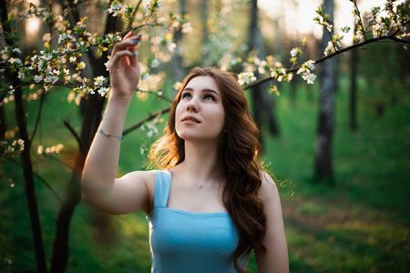Beautiful young girl in a blue dress in a spring park.の写真素材