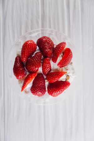 Strawberry dessert in a plate with ice cream and cream on a white wooden background.の写真素材