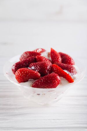 Strawberry dessert in a plate with ice cream and cream on a white wooden background.の写真素材