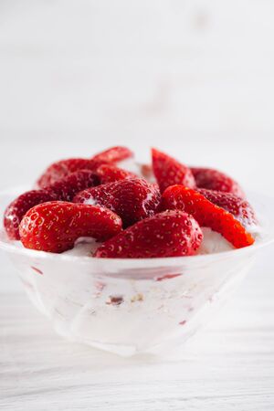 Strawberry dessert in a plate with ice cream and cream on a white wooden background.の写真素材