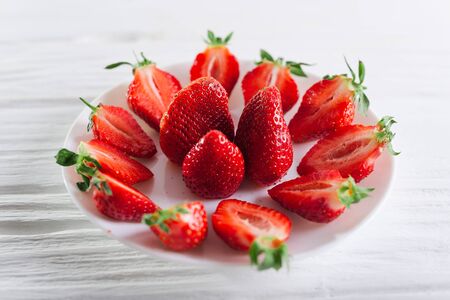 Juicy fresh sliced strawberries on a white plate on a white wooden background.の写真素材