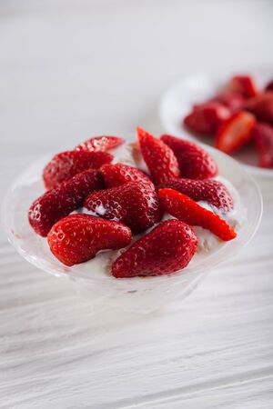 Strawberry dessert in a plate with ice cream and cream on a white wooden background.の写真素材