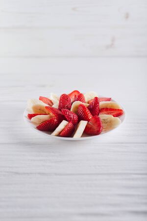 Juicy fresh sliced strawberries with banana on a white plate on a white wooden background.の写真素材