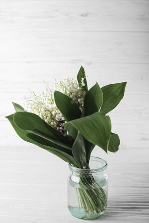 Lilies of the valley in a glass jar on a white wooden background.の写真素材