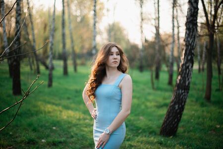 Beautiful young girl in a blue dress in a spring park.の写真素材